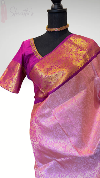 Authentic kanjivaram saree available in USA ready to ship with stitched blouse A pink and purple kanchi silk saree with gold zari embroidery stitched blouse The blouse is a vibrant magenta with gold border detailing, and the saree body features a pink and purple floral pattern with a wide gold border.