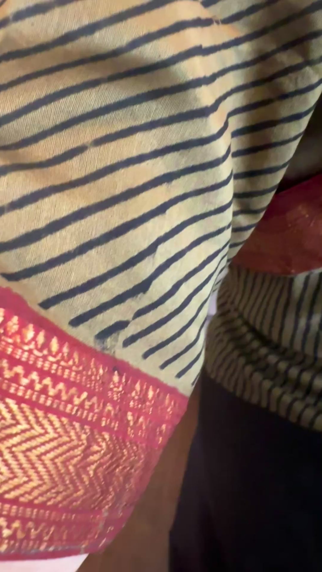 Maheshwari silk cotton saree showing fine black and gold stripes with a rich red zari border, highlighting the smooth texture and handwoven detailing.